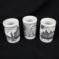 Set of three vintage Bremen Germany porcelain shot glasses arranged against a black background. The white cylindrical cups feature black architectural illustrations labeled Bremen Der Roland, Bremen Stadtmusikanten, and Bremen Rathaus, with their open rims visible.