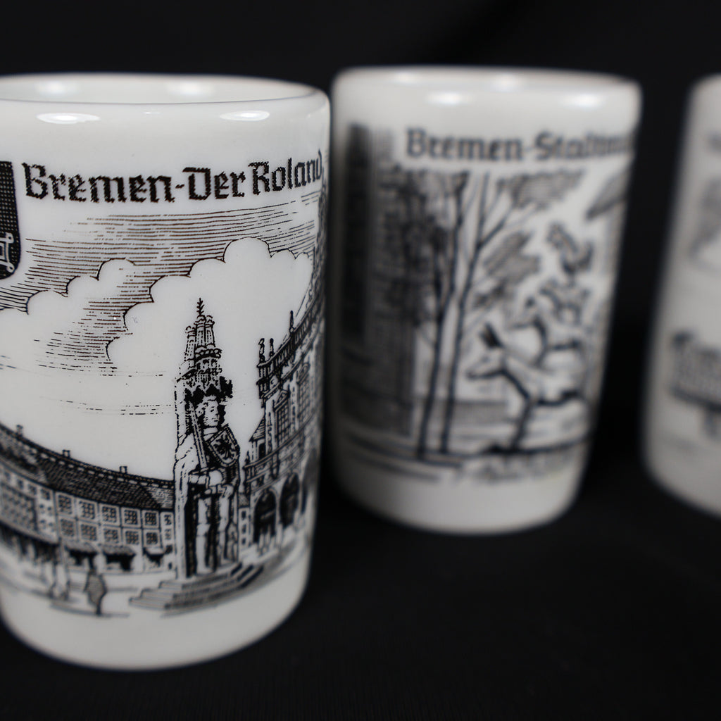 Close-up photograph focused on the vintage Bremen Der Roland porcelain shot glass. The black-and-white design shows the standing Roland statue and surrounding marketplace architecture, while the Town Musicians and Rathaus cups appear softly blurred in the background.