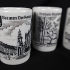 Close-up photograph focused on the vintage Bremen Der Roland porcelain shot glass. The black-and-white design shows the standing Roland statue and surrounding marketplace architecture, while the Town Musicians and Rathaus cups appear softly blurred in the background.
