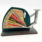 Elevated front view of a Brower-branded Jiffy-Way egg scale on white, showing the colorful sizing chart, open pointer and shallow metal cup. The cup’s interior has mottled discoloration, and the rectangular green base shows extensive brown surface rust.