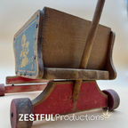 Low rear angle of the vintage wooden Cass Toys doll stroller displaying the sturdy undercarriage, rear push handle, solid wood body, and original painted finish with vintage character.