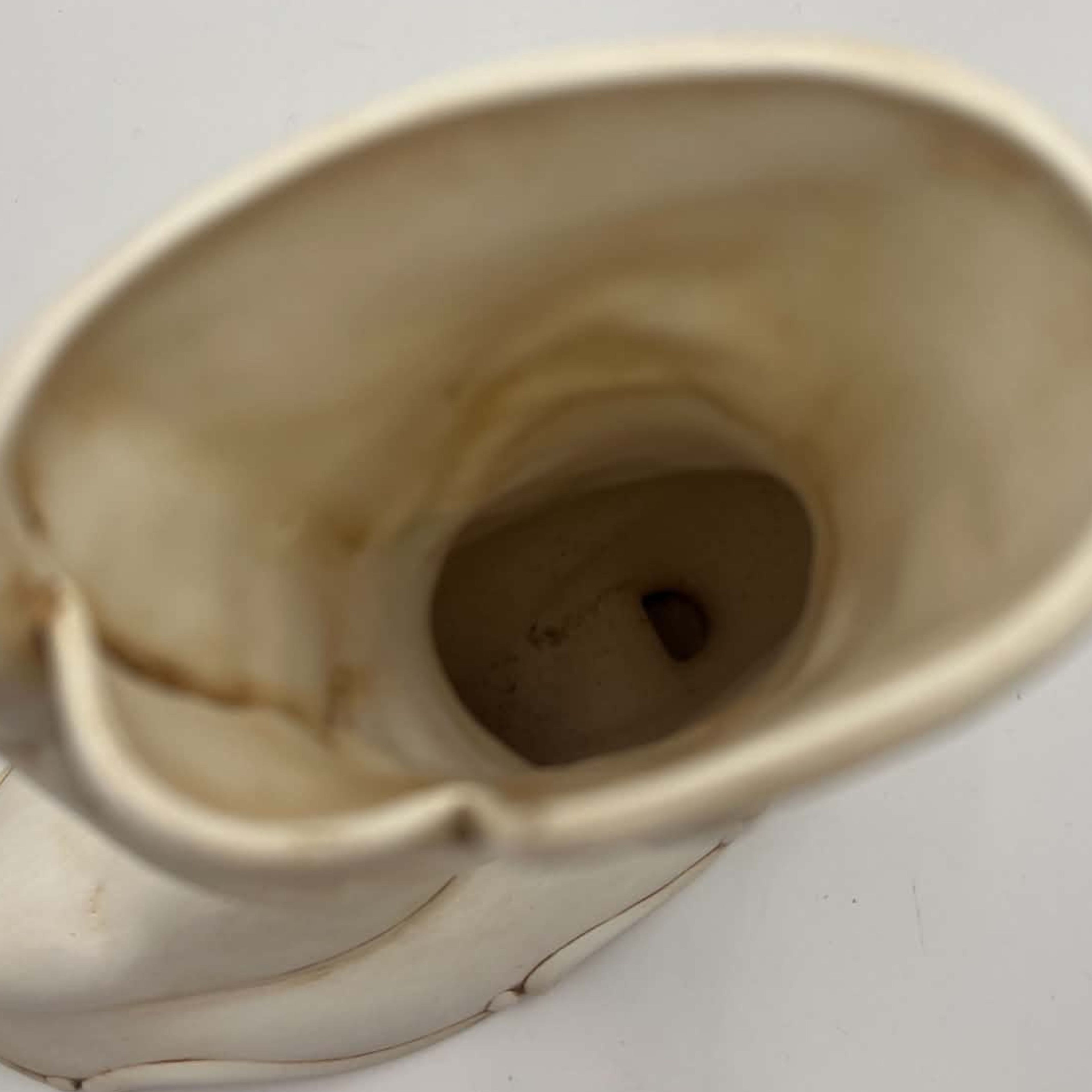 View inside the open shaft of a vintage Atlantic Mold ceramic boot planter. The photograph documents the cream-colored interior, age-related discoloration, surface marks and recessed opening near the bottom, helping shoppers assess its construction and previous use.