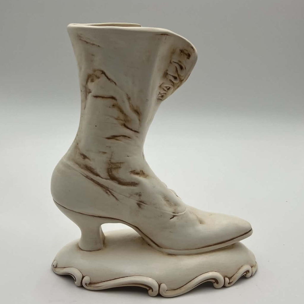 Opposite side of a vintage ivory ceramic Victorian boot planter, showing its tall curved shaft, pointed toe, narrow heel and ornamental pedestal. Hand-applied brown accents settle into the sculpted creases and edges, creating an intentionally antiqued appearance.