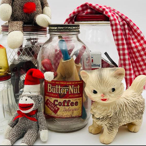 Vintage sock monkeys, a cream cat figurine, glass kitchen jars, a Butter-Nut coffee tin and red gingham fabric arranged together, representing the nostalgic objects and collected stories featured in the Zestful Productions vintage blog.