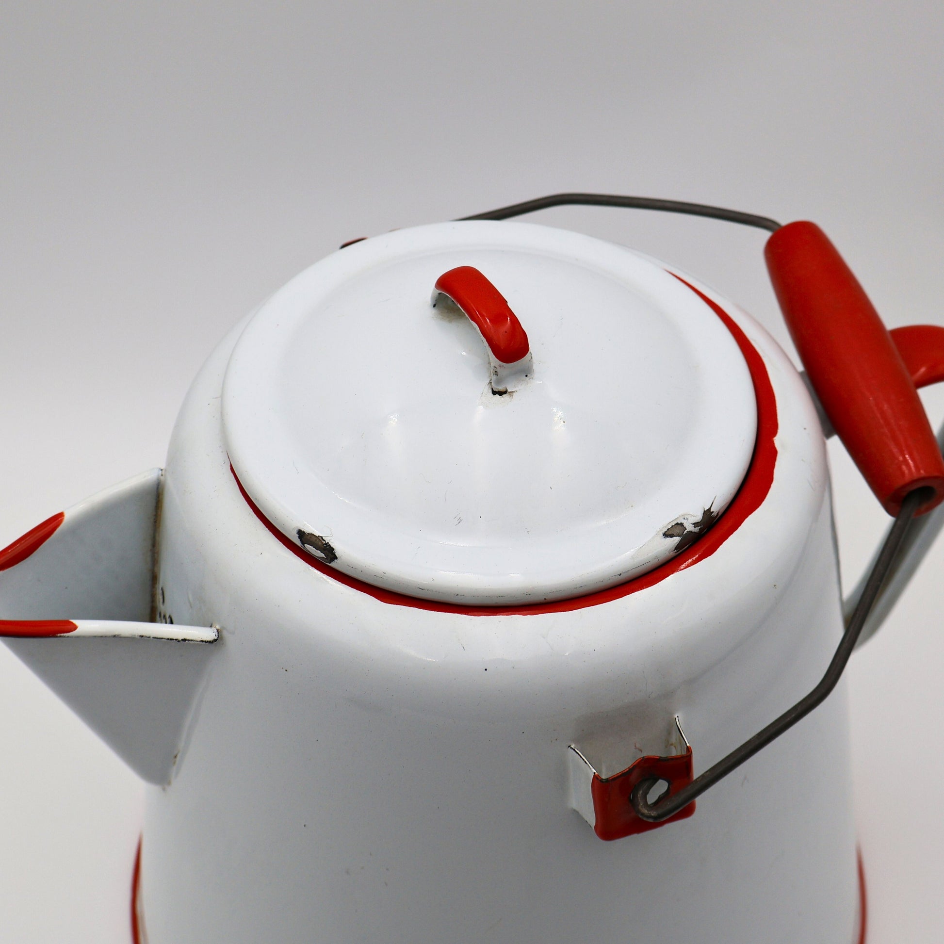 Close up of red trimmed lid on large antique enamel coffee pot with light chipping