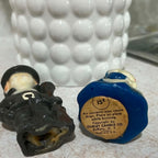 Underside view of vintage Gurley pilgrim candles showing the female figure's original round paper label marked 15 cents, Gurley Candle Co., Buffalo New York and Made in USA. The male figure's molded wax base and lower gun detail are visible beside the labeled candle.