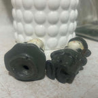 Underside condition view of two vintage Gurley Thanksgiving pilgrim candles lying on their backs, showing the molded wax bases and small openings underneath. The photograph also documents the unburned figures, cream faces, dark clothing and vintage surface wear.