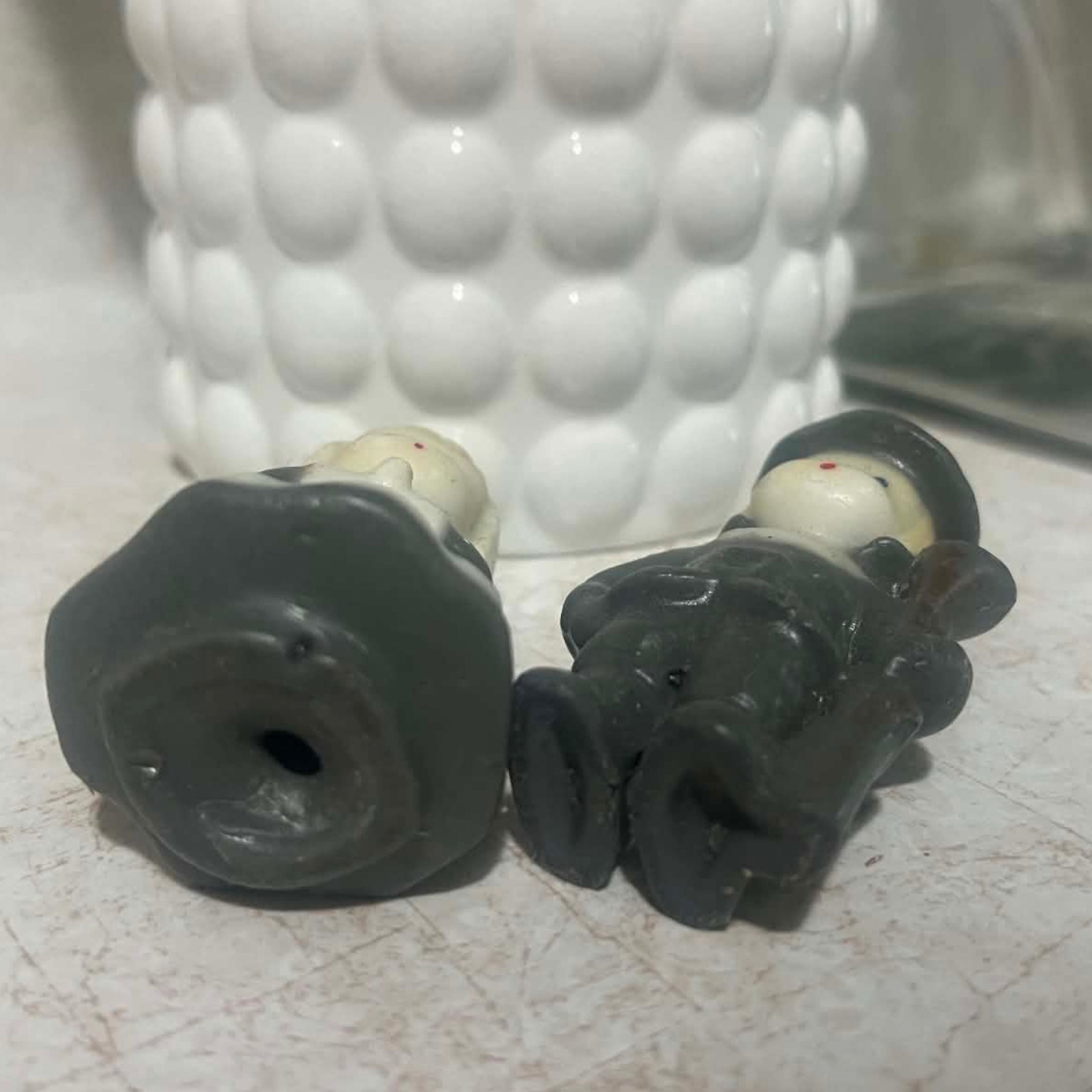 Underside condition view of two vintage Gurley Thanksgiving pilgrim candles lying on their backs, showing the molded wax bases and small openings underneath. The photograph also documents the unburned figures, cream faces, dark clothing and vintage surface wear.