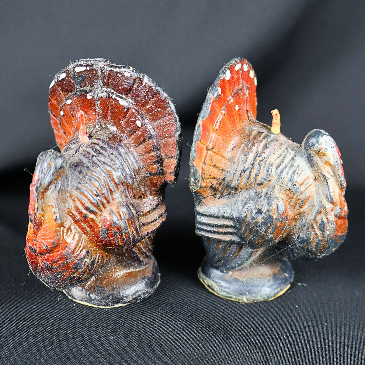 Pair of vintage Gurley turkey candles displayed together against a black background. The small molded wax Thanksgiving figures have rounded brown and black bodies, red-orange tail feathers, painted white accents, upright wicks and circular bases with visible age-related wear.