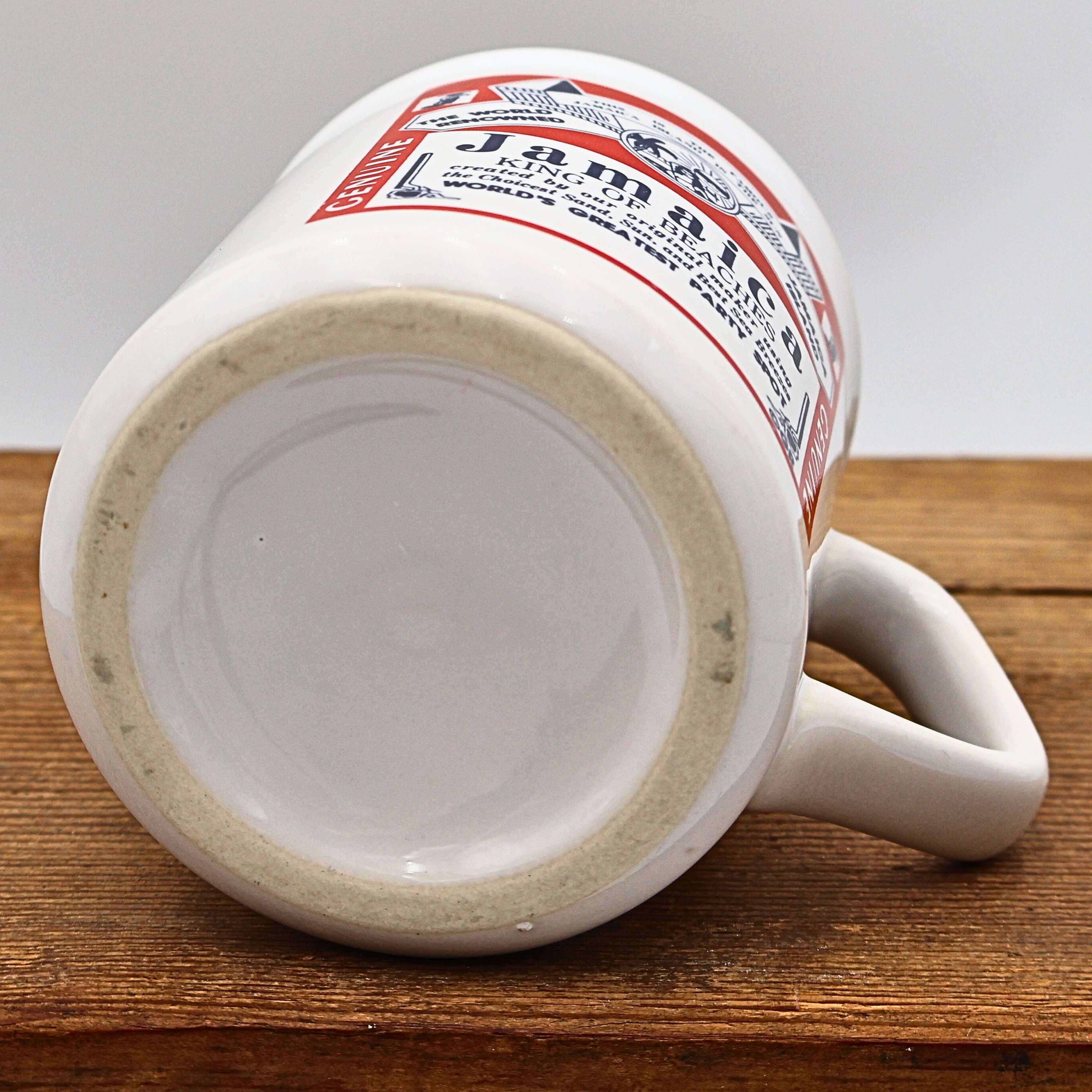 Bottom view of the vintage ceramic Jamaica souvenir mug showing the unmarked glazed base with exposed foot ring. The underside displays normal wear consistent with age and confirms the overall construction of this collectible travel coffee mug.