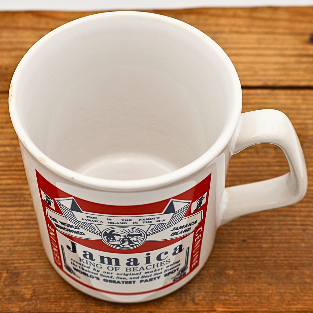 Top angled view inside the vintage Jamaica souvenir coffee mug showing the clean white glazed interior together with the colorful front graphic. The photograph illustrates the approximate eleven-ounce capacity and overall vintage condition of the ceramic mug.