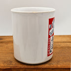 Opposite side angle of the vintage Jamaica travel coffee mug showing the transition between the plain ceramic body and the colorful beer label-inspired souvenir graphic. Minor rim wear is visible while the glossy finish remains attractive throughout the mug.