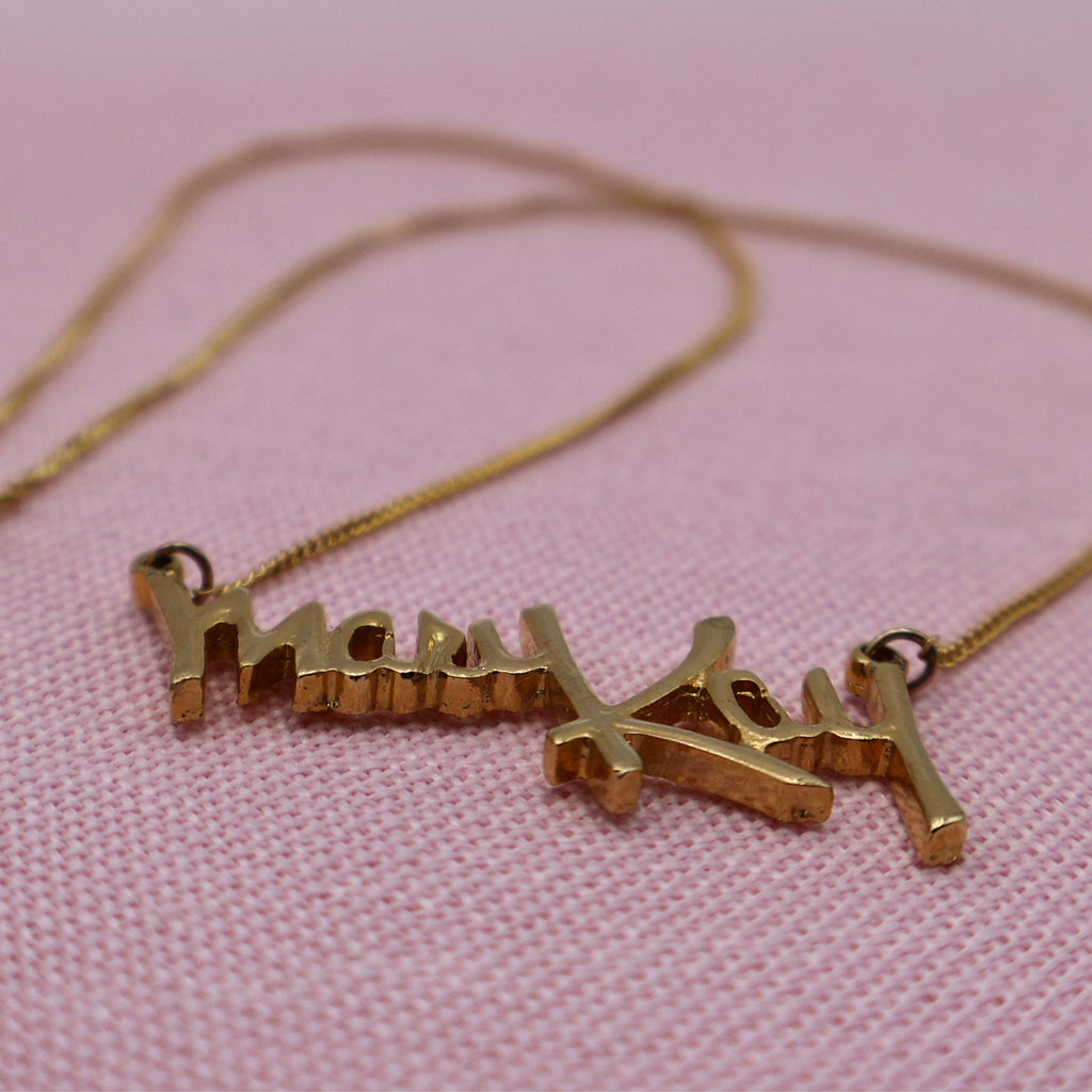 Side angle of vintage Mary Kay distributor necklace showing raised gold script pendant detail and chain.