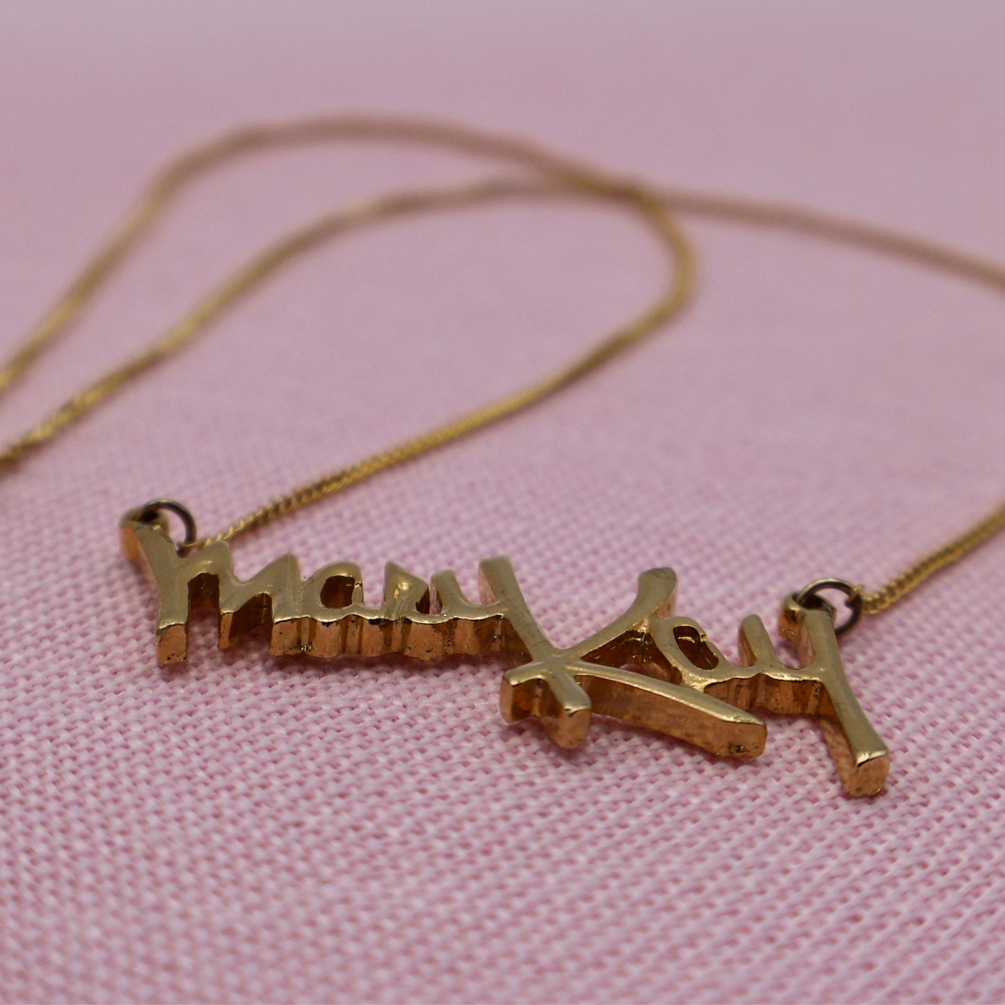 Side angle of vintage Mary Kay distributor necklace showing raised gold script pendant detail and chain.