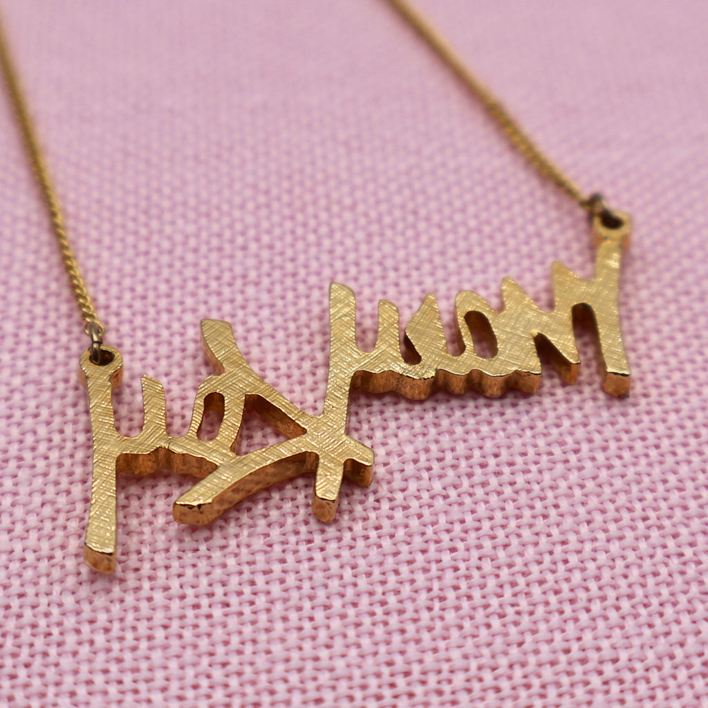 Back side detail of vintage Mary Kay gold tone script pendant showing textured finish and craftsmanship.