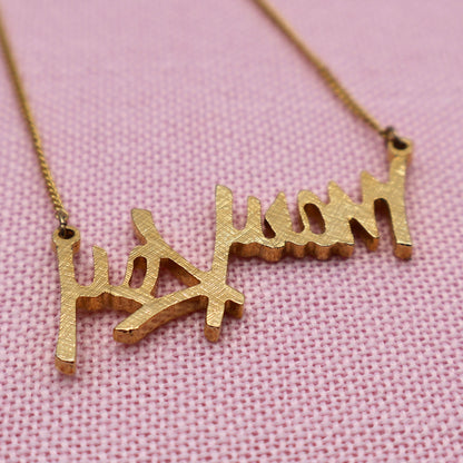 Back side detail of vintage Mary Kay gold tone script pendant showing textured finish and craftsmanship.