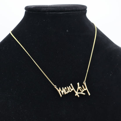 Vintage Mary Kay gold tone script pendant necklace displayed on black mannequin bust, retro direct sales jewelry.