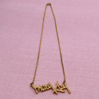 Full length view of vintage Mary Kay signature necklace with gold tone chain and script pendant on pink fabric background.