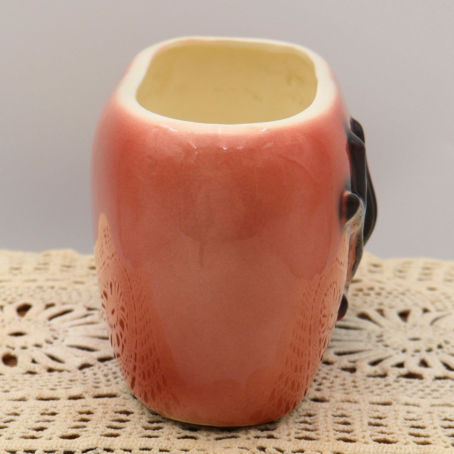Side view of mid-century Royal Copley pink pottery planter with sculptural black leaf accent.