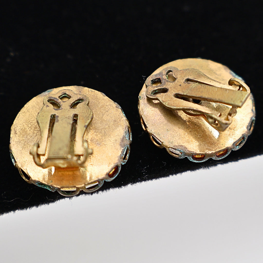 Reverse view of vintage Mount Rushmore clip-on earrings showing unmarked gold-tone backs and classic clip closures for non-pierced ears. The photograph documents the construction, hardware, and overall vintage condition of this mid-century souvenir jewelry pair.