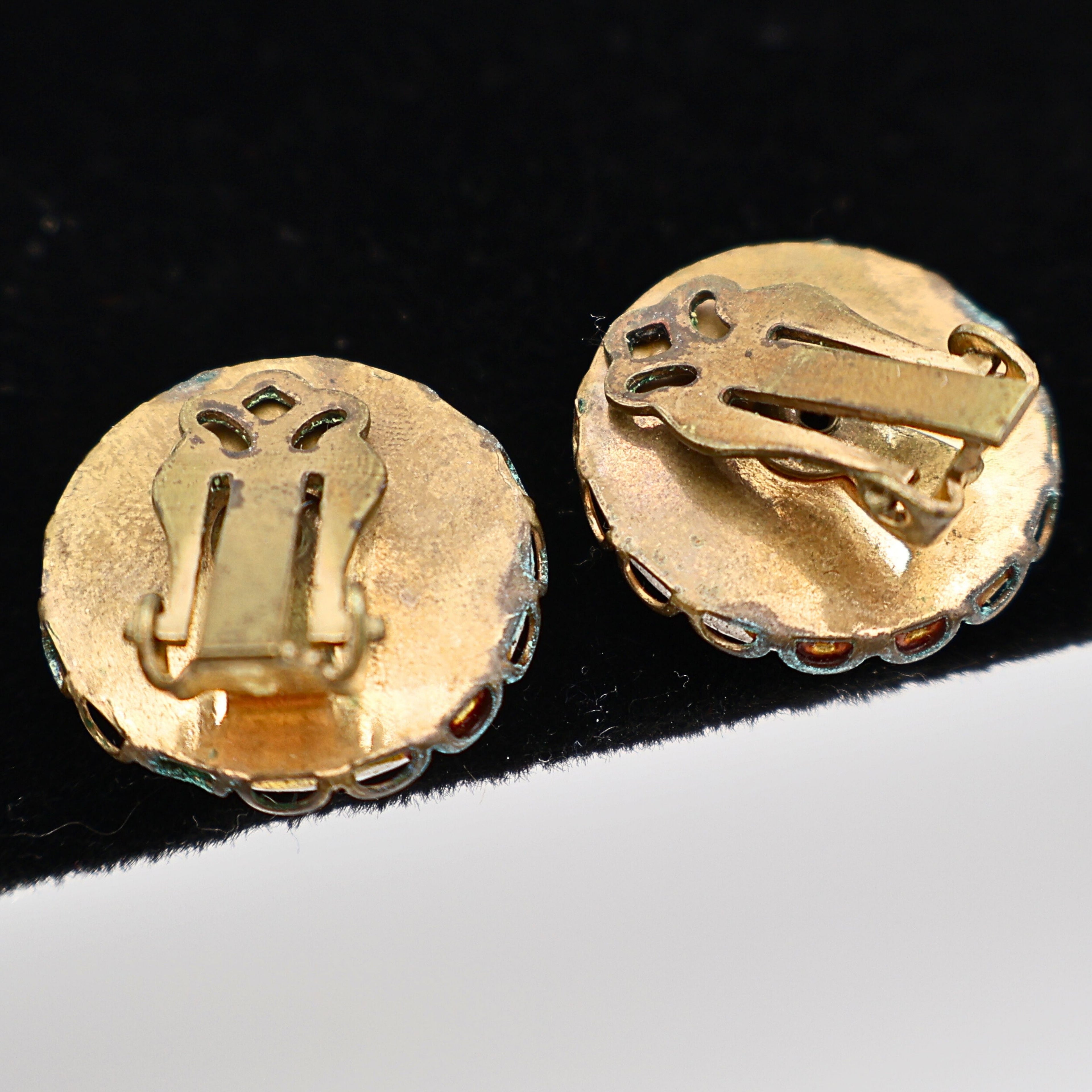 Reverse view of vintage Mount Rushmore clip-on earrings showing unmarked gold-tone backs and classic clip closures for non-pierced ears. The photograph documents the construction, hardware, and overall vintage condition of this mid-century souvenir jewelry pair.