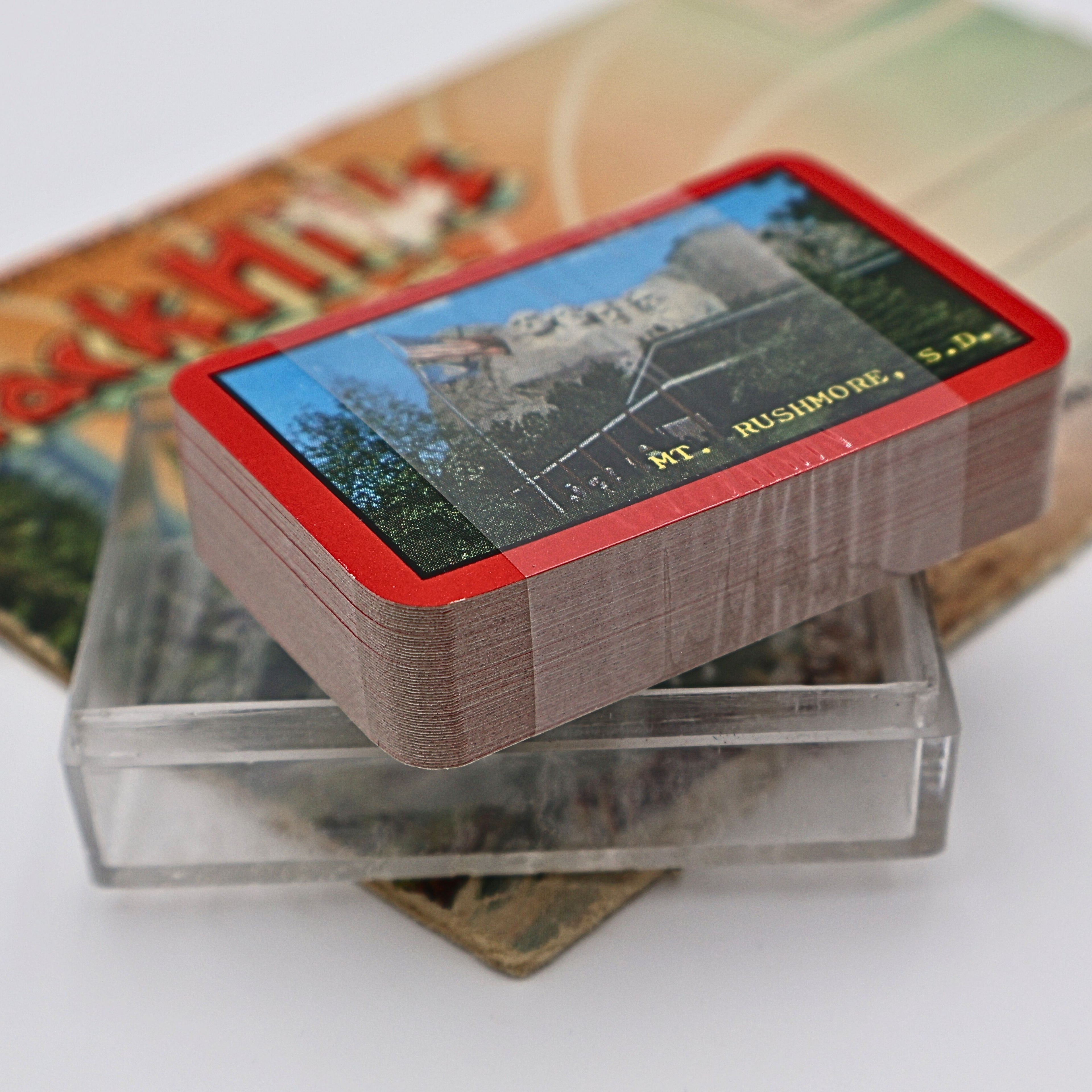 Vintage Mount Rushmore souvenir playing cards resting inside the original clear plastic display case. The unopened deck showcases the scenic Mount Rushmore card back artwork while highlighting its preserved condition and nostalgic roadside souvenir charm.