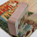 Side profile of the unopened vintage Mount Rushmore souvenir playing card deck showing the tightly stacked card edges beneath the factory plastic wrap. The compact travel-sized deck illustrates its preserved unused condition and collectible appeal.