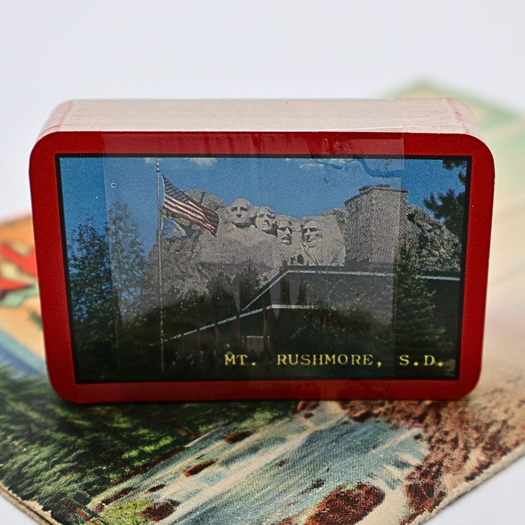 Vintage Mount Rushmore souvenir playing cards displayed with plastic seal with the deck standing upright. The sealed playing cards feature colorful Mount Rushmore artwork and remain an appealing collectible for travel memorabilia enthusiasts.