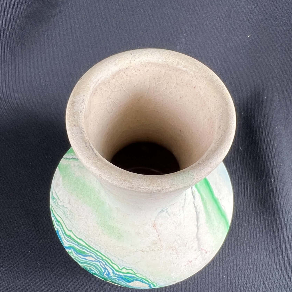 Overhead view of a small Nemadji pottery vase on black fabric, showing a wide cream-colored rim, a narrow interior opening and fine lines near the inner mouth. Green and blue marbled bands curve around the pale, softly rounded body beneath the flared neck.