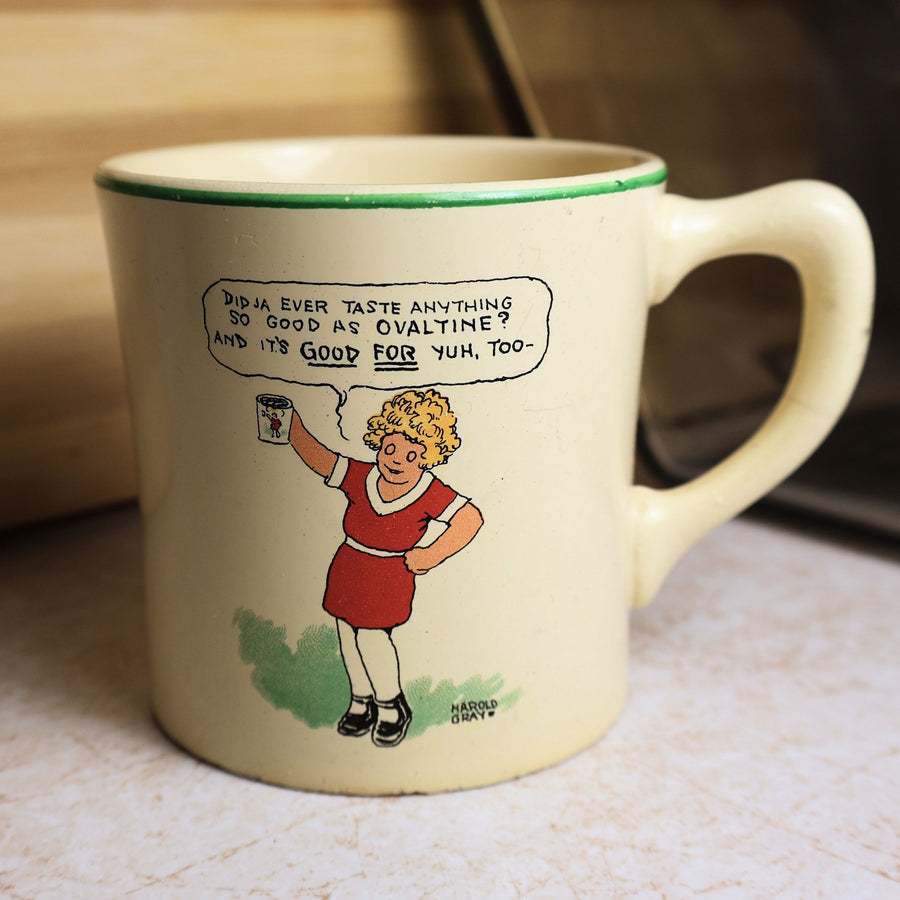 Vintage Ovaltine ceramic advertising mug featuring Harold Gray artwork of a young girl holding Ovaltine with a humorous speech bubble and green rim.