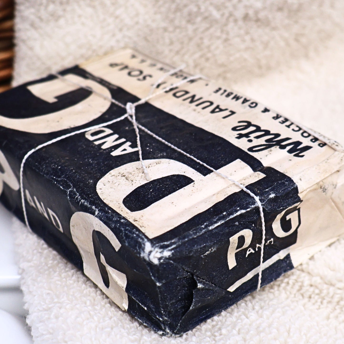 Angled view of an authentic World War II era P&G White Laundry Soap bar showing the original paper wrapper, folded corners, and age-related wear. This vintage Procter & Gamble advertising collectible makes a unique display piece for primitive farmhouse decor, vintage laundry rooms, and Americana collections.