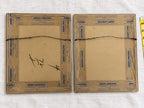 Rear view of both framed prints with brown paper backing, Jenson’s Upholstery printed tape, and attached wire hangers. One backing has large handwritten marks, and both show age-related spots. Part of a yellow measuring tape appears along the right edge.