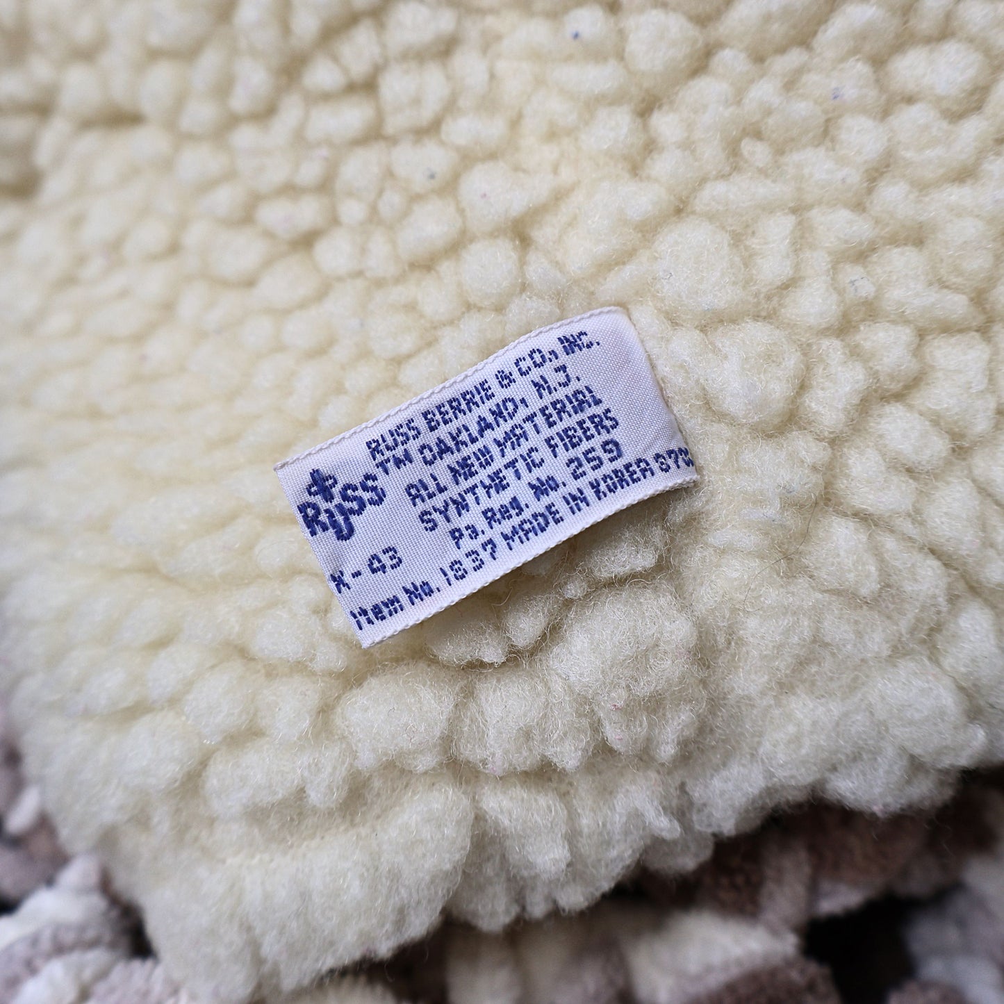 Detailed close-up of the original Russ Berrie manufacturing tag attached to the vintage Snuggle Bear hand puppet. The tag confirms production details and adds collectible value for fans of vintage plush toys and advertising memorabilia.