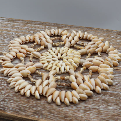 Vintage 9 inch seashell trivet made from cowrie and puka shells in starburst design on wood table