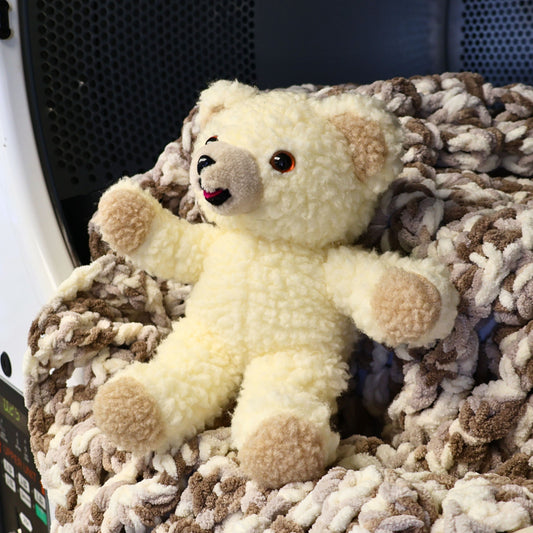Vintage 1996 Snuggle Bear plush by Lever Brothers Company sitting with open arms on a soft knit blanket. This 10-inch fabric softener mascot features fluffy cream sherpa fur, bright amber eyes, and a cheerful smile, making it a wonderful vintage advertising collectible and nostalgic home decor accent.