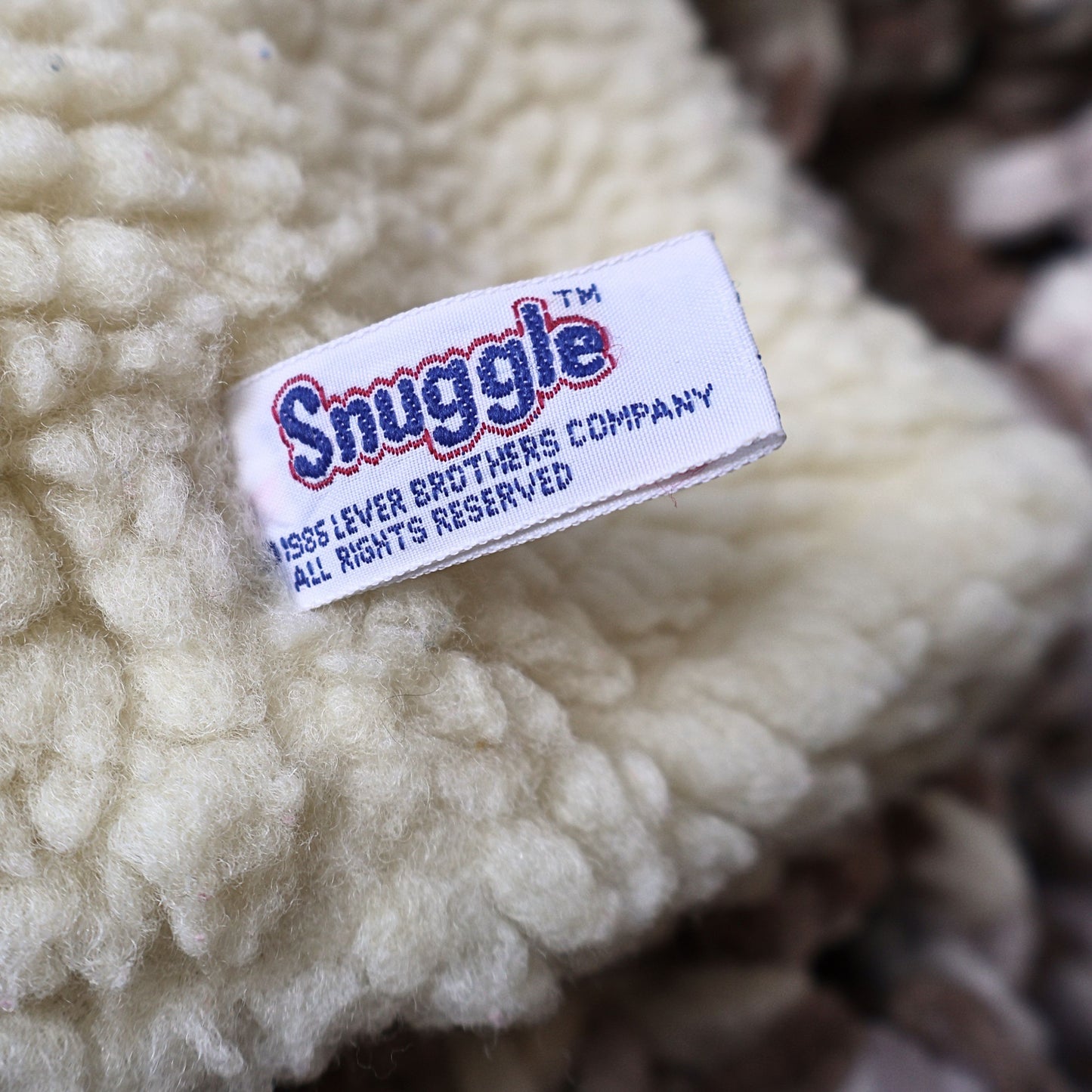 Close-up photograph of the original Snuggle brand tag attached to the vintage 1986 hand puppet, identifying Lever Brothers Company. Original manufacturer tags add authenticity and collector appeal for vintage advertising enthusiasts.