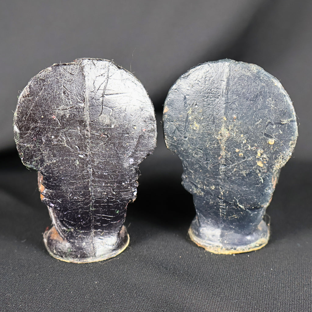Rear view of two vintage Gurley figural turkey candles against black fabric. Their broad, flattened tail backs and rounded pedestal bases are coated in dark brown and black wax, with numerous scratches, rubbed areas, embedded lint and other visible signs of age and handling.