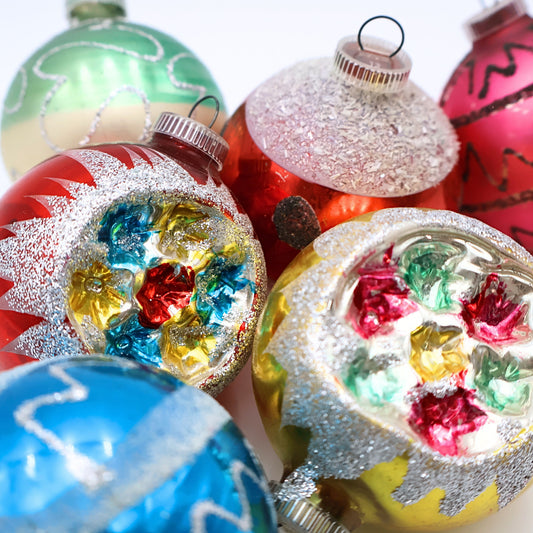 Closeup of vintage West Germany reflector Christmas ornaments featuring colorful floral indents, silver mica glitter, and mid century mercury glass decoration