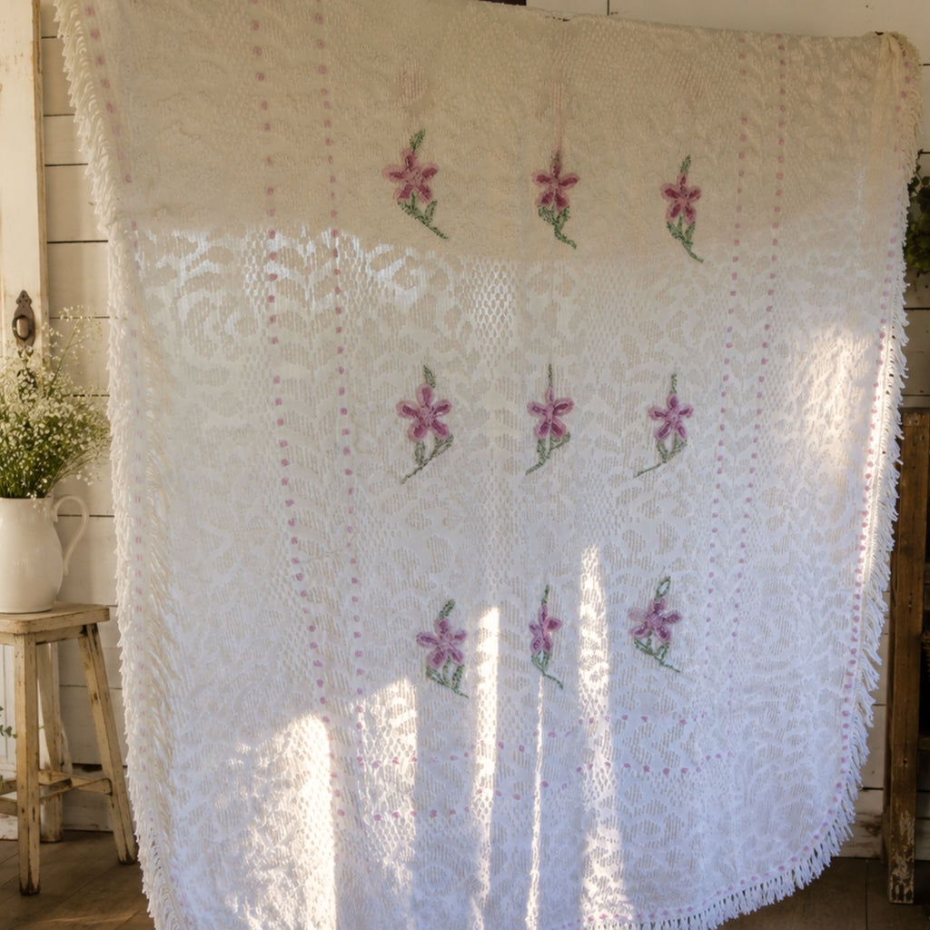 Vintage white chenille bedspread with lavender floral hand-tufted design displayed in a cottage-inspired room. This heirloom textile features decorative fringe and raised chenille texture, making it a beautiful choice for farmhouse decor, shabby chic bedrooms, romantic bedding, and vintage home decorating.