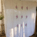 Vintage white chenille bedspread with lavender floral hand-tufted design displayed in a cottage-inspired room. This heirloom textile features decorative fringe and raised chenille texture, making it a beautiful choice for farmhouse decor, shabby chic bedrooms, romantic bedding, and vintage home decorating.