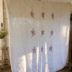 Vintage white chenille bedspread with lavender floral hand-tufted design displayed in a cottage-inspired room. This heirloom textile features decorative fringe and raised chenille texture, making it a beautiful choice for farmhouse decor, shabby chic bedrooms, romantic bedding, and vintage home decorating.