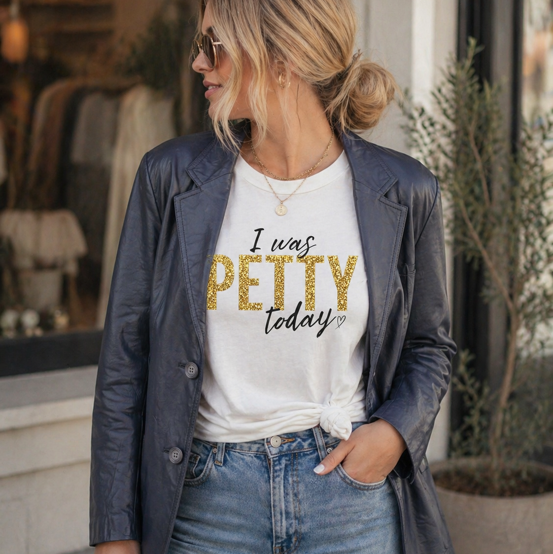 A woman wearing a vintage gray leather blazer styled over a white “I Was Petty Today” graphic t-shirt with gold lettering, paired with casual denim jeans for a bold, playful street-style outfit.