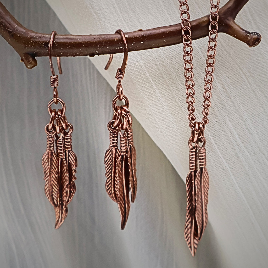 Vintage Y2K feather jewelry set displayed on rustic branch featuring copper tone dangle earrings and matching feather pendant necklace, boho western style jewelry set with nature inspired feather charms, lightweight statement earrings and dainty necklace gift for her, festival jewelry and vintage costume accessory with warm copper finish