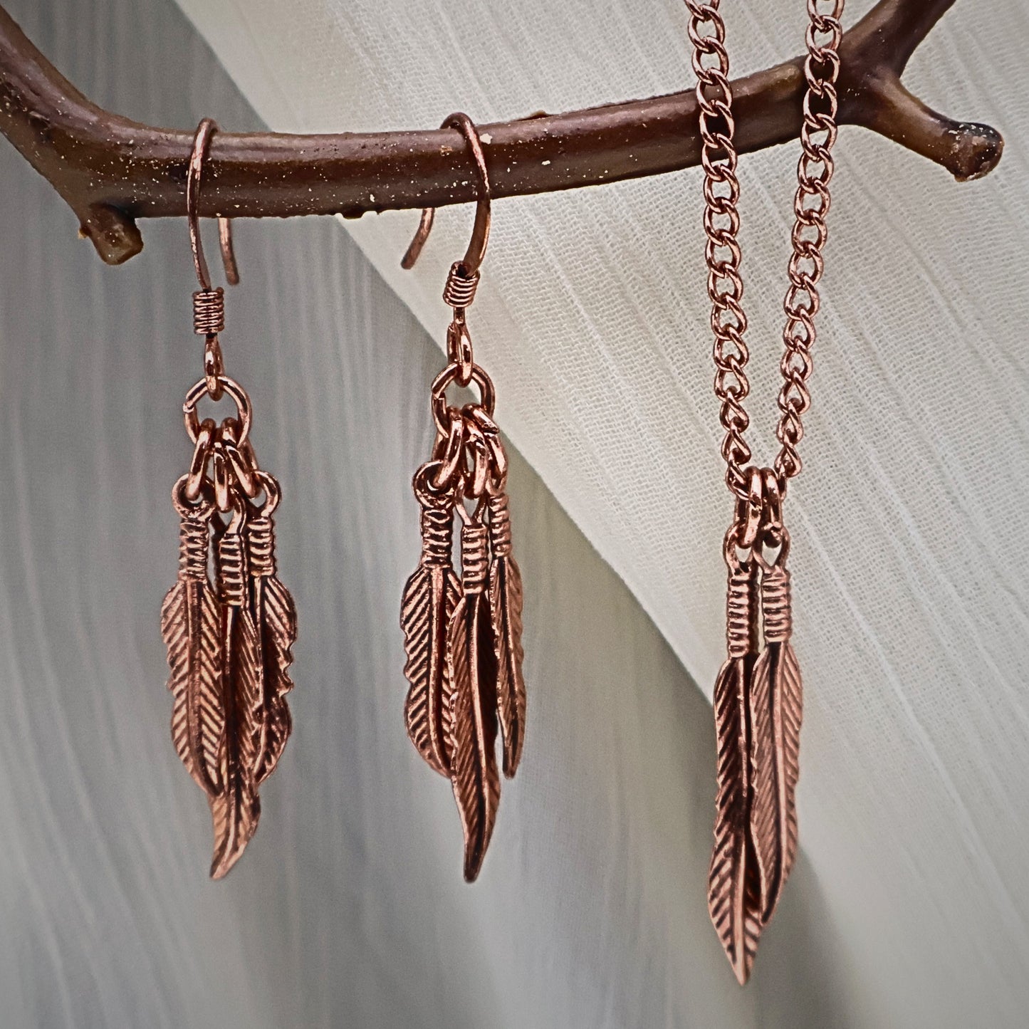 Vintage Y2K feather jewelry set displayed on rustic branch featuring copper tone dangle earrings and matching feather pendant necklace, boho western style jewelry set with nature inspired feather charms, lightweight statement earrings and dainty necklace gift for her, festival jewelry and vintage costume accessory with warm copper finish