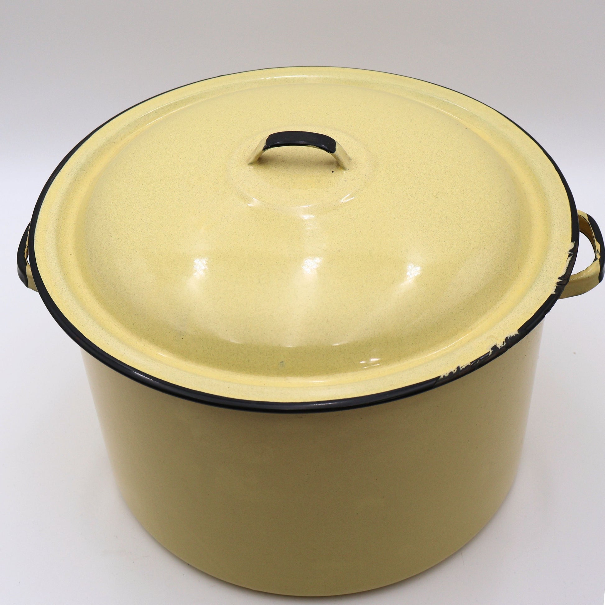 Angled front view of a vintage yellow enamelware stock pot with matching lid showcasing its classic farmhouse silhouette, black trim, and warm buttery yellow finish. A timeless piece for cottagecore décor, vintage kitchen collections, and rustic home styling.