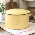 Vintage yellow enamelware stock pot with matching lid styled in a rustic farmhouse kitchen beside a sunny window. This large mid-century enamelware cooking pot features a buttery yellow finish with black trim and adds timeless charm to farmhouse, cottagecore, country, and vintage-inspired home decor.