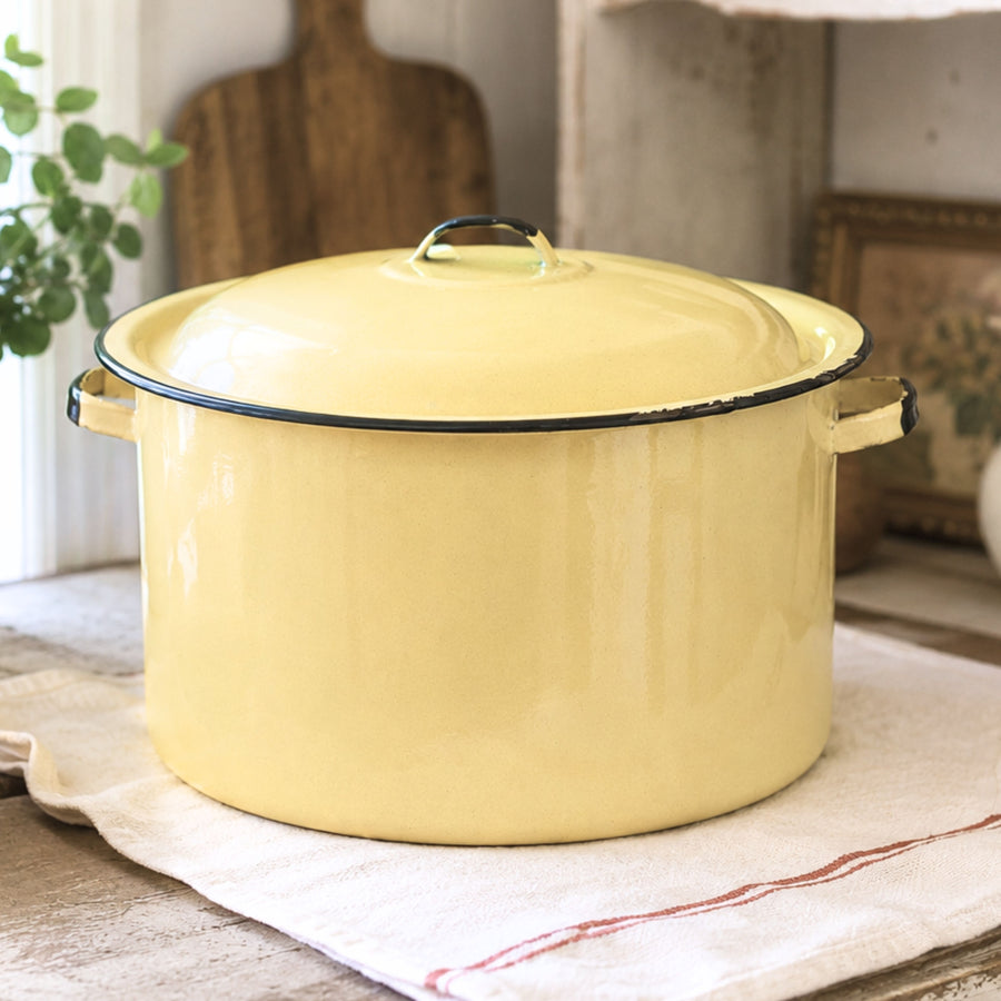 Vintage yellow enamelware stock pot with matching lid styled in a rustic farmhouse kitchen beside a sunny window. This large mid-century enamelware cooking pot features a buttery yellow finish with black trim and adds timeless charm to farmhouse, cottagecore, country, and vintage-inspired home decor.