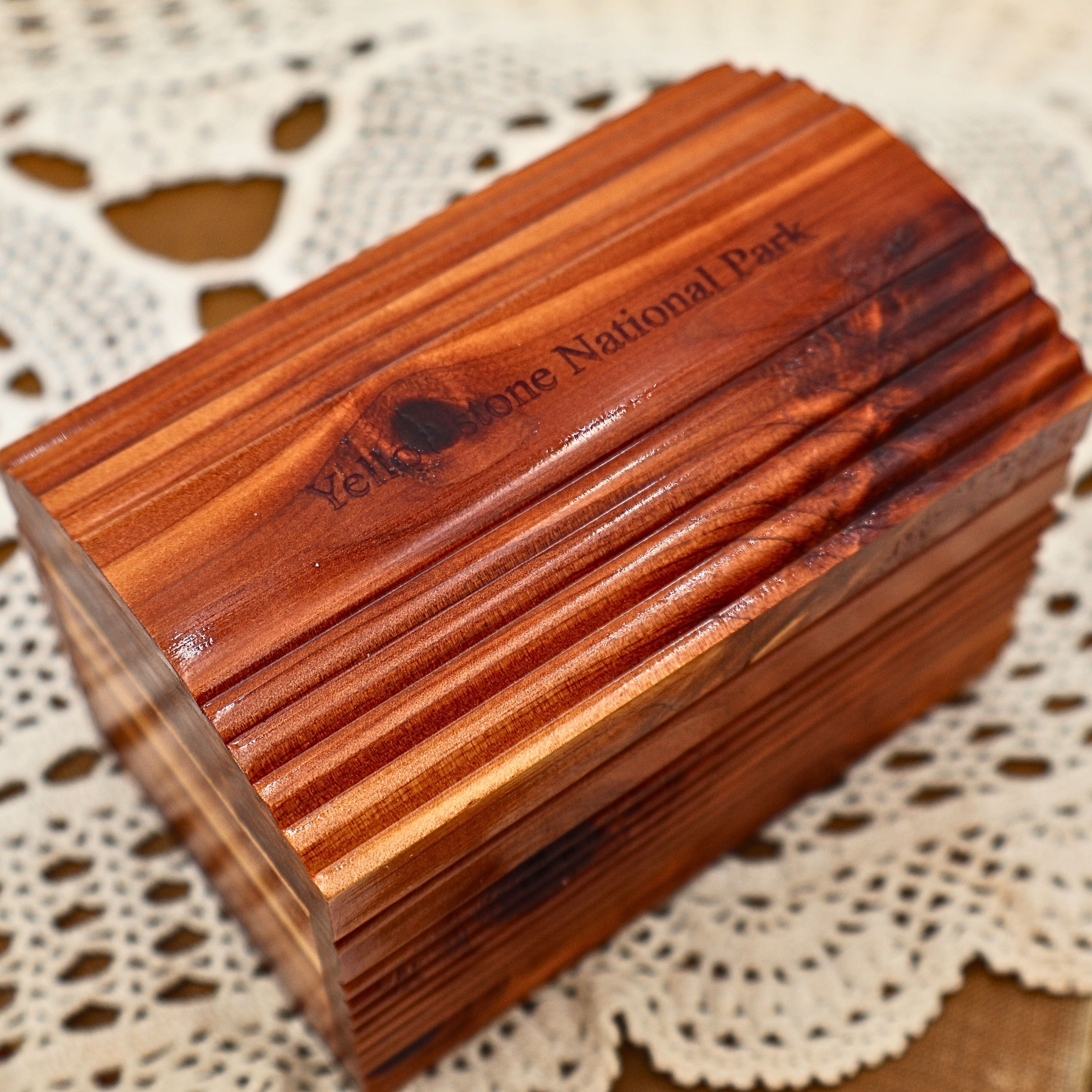 Close-up view of the vintage Yellowstone National Park cedar keepsake box showing the engraved park name across the arched lid. Rich natural cedar grain, distinctive knots, and decorative ribbed carving highlight the craftsmanship of this classic wooden souvenir chest.