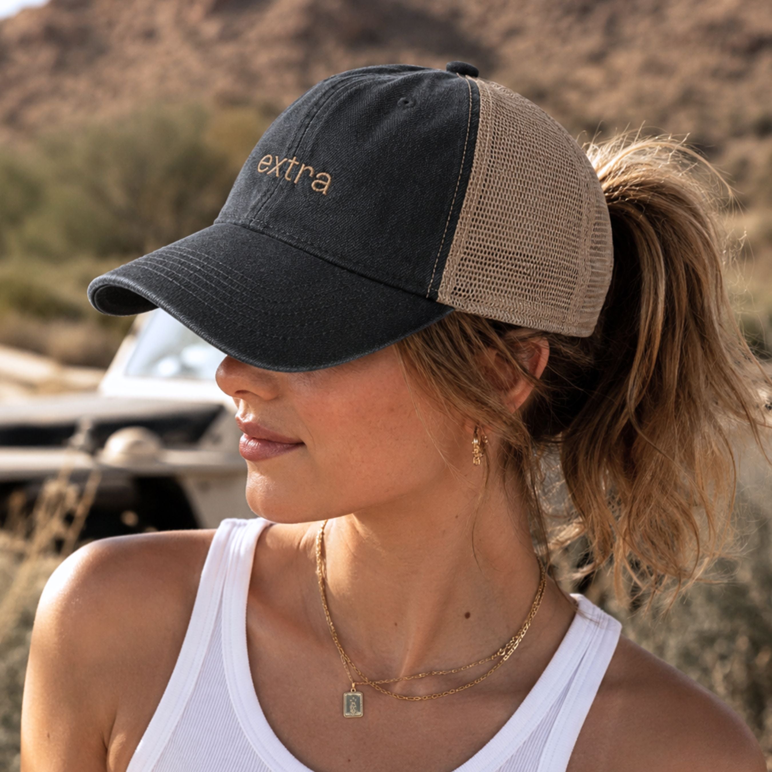 Woman wearing washed black mesh back ponytail trucker hat with messy bun opening and leopard underbrim detail outdoors