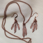Complete feather jewelry set with copper tone necklace and dangle earrings arranged in styled flat lay, western boho jewelry with nature inspired feather design, statement necklace paired with lightweight earrings, gift for her perfect for country western outfits, festival looks and vintage style costume jewelry